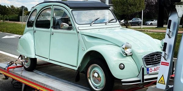 Mintgroene Citroen 2CV oldtimer vastgezet op het laadplatform langs een straat in zacht zomerlicht
